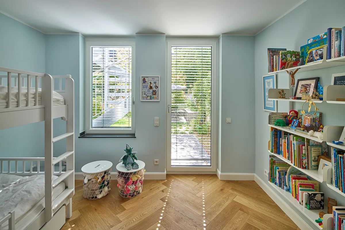 Kinderzimmer im Untergeschoss der Maisonettewohnung mit hellblauen Wänden, Eichenparkett und Zugang zum Garten.